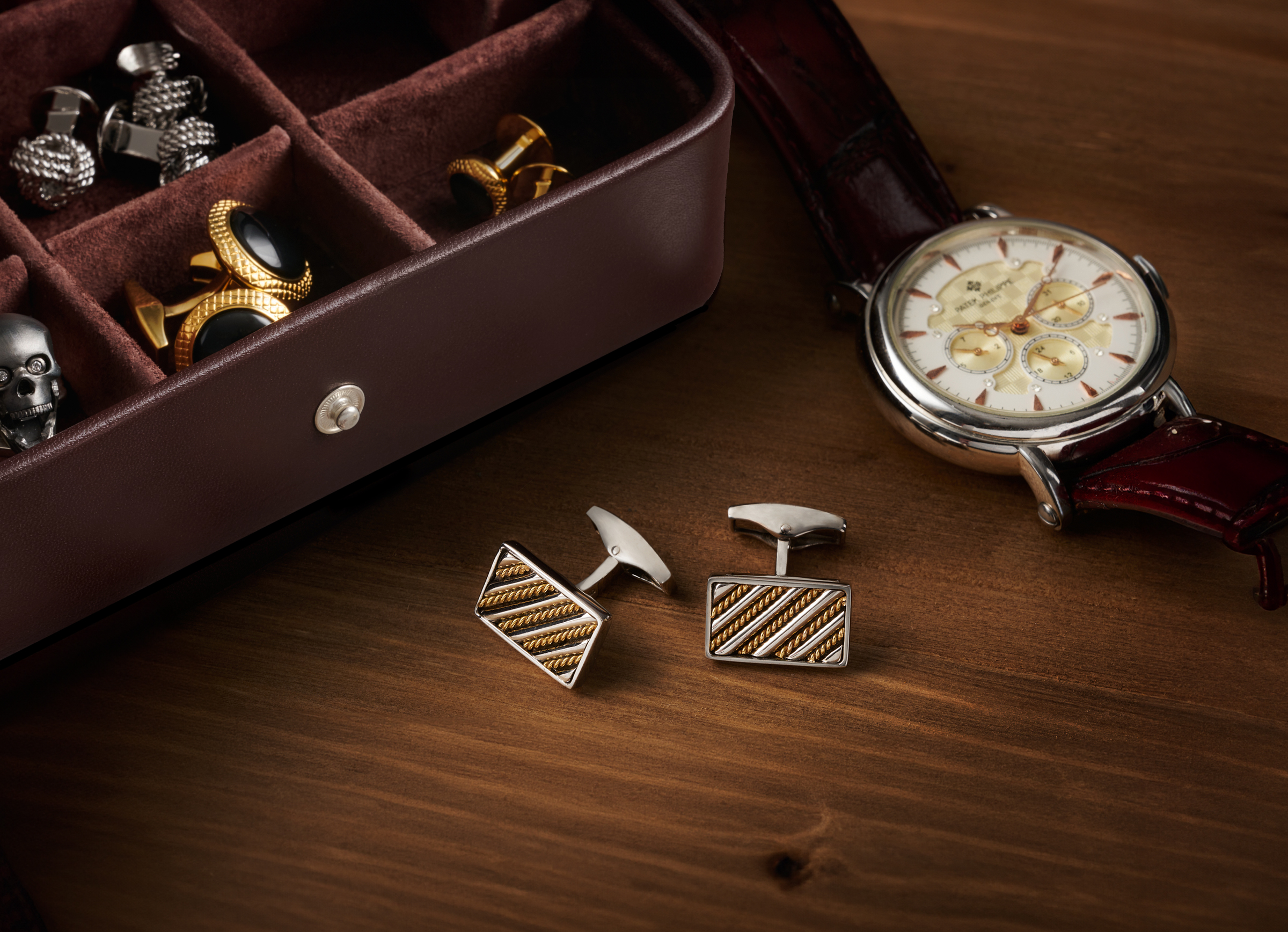 Luxury Cufflinks on a wood table with a jewelry case and luxury watch.