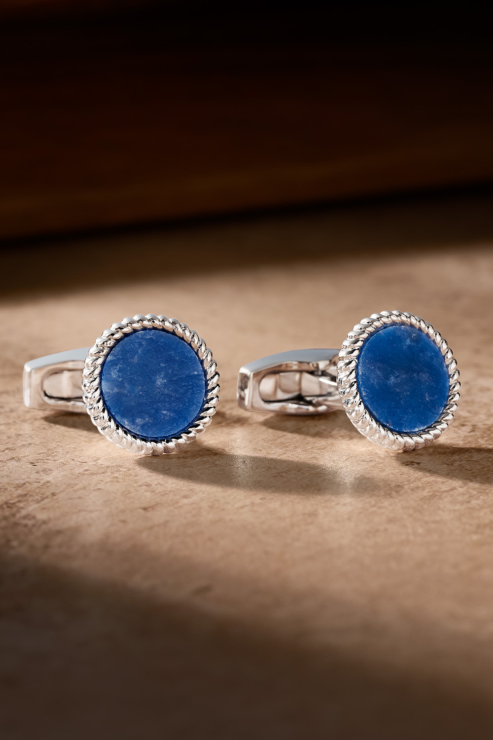 Blue sodalite and silver cufflinks on a tan table.