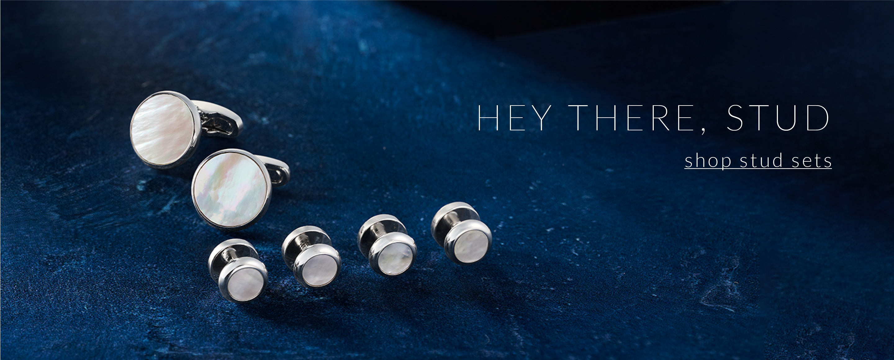 Shop Stud Sets. Mother of Pearl and silver stud set on a blue background.