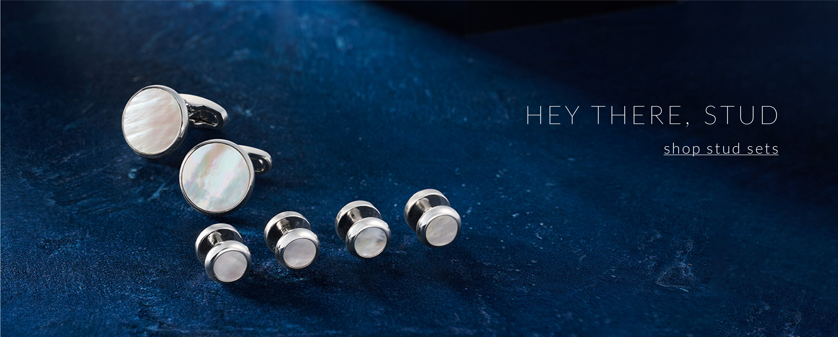 Shop Stud Sets. Mother of Pearl and silver stud set on a blue background.