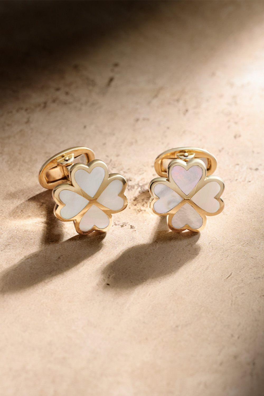 Mother of pearl and gold clover cufflinks on a tan table.