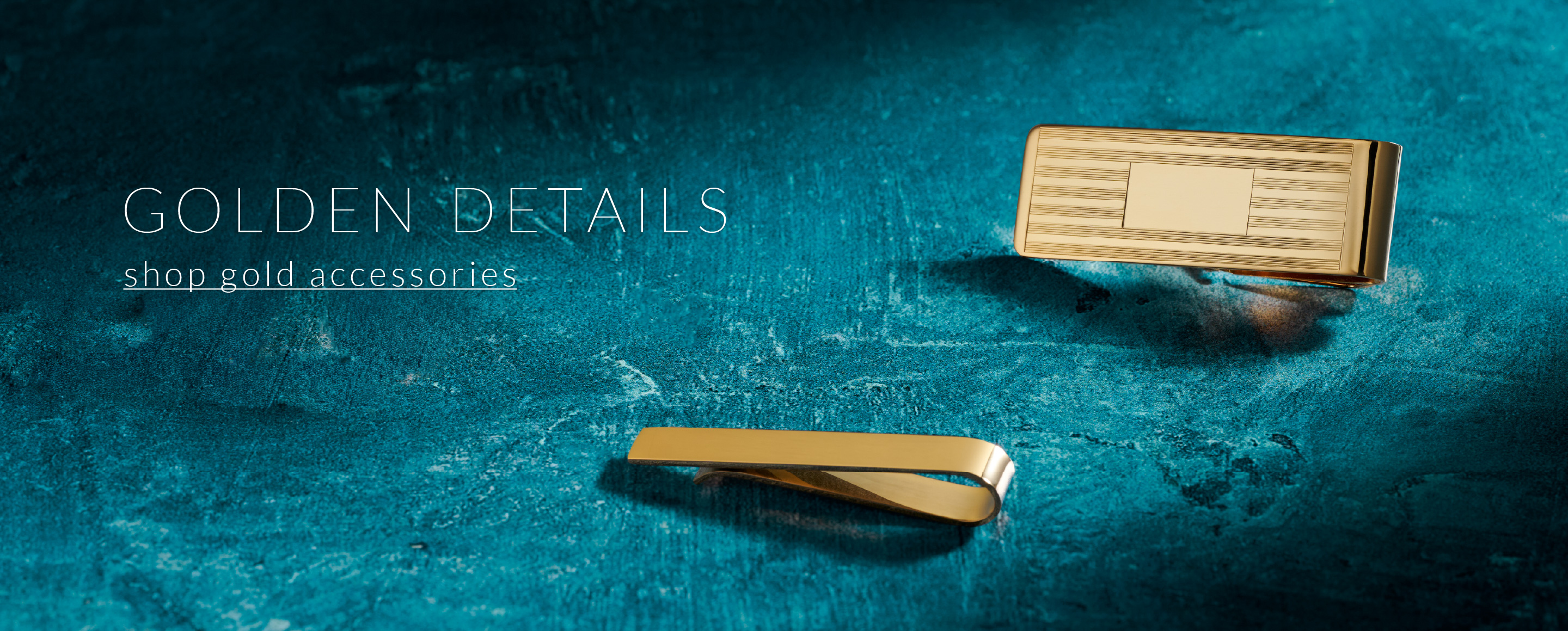 Shop Gold Accessories. Gold money clip and gold tie bar on a blue-green background.