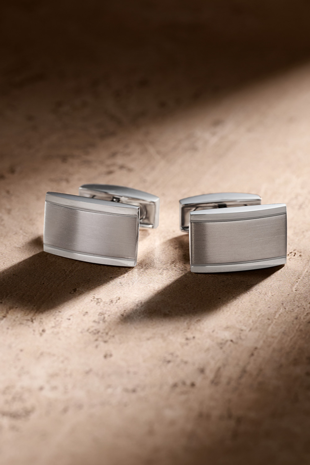Silver cufflinks on a tan background.