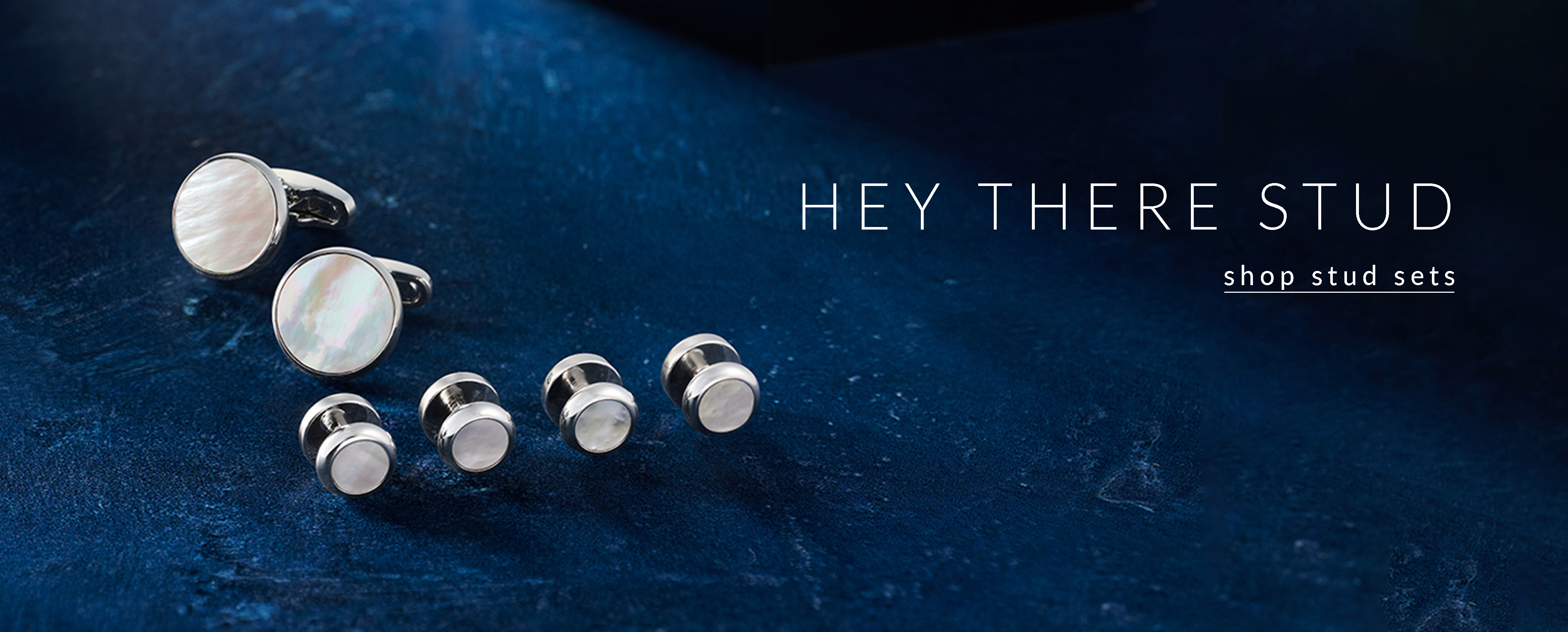 Shop Stud Sets. Mother of Pearl and silver stud set on a blue background.